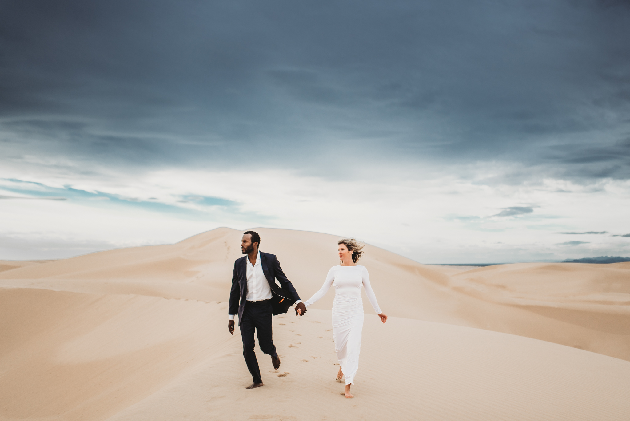 wedding couple running across sand dunes under stormy sky