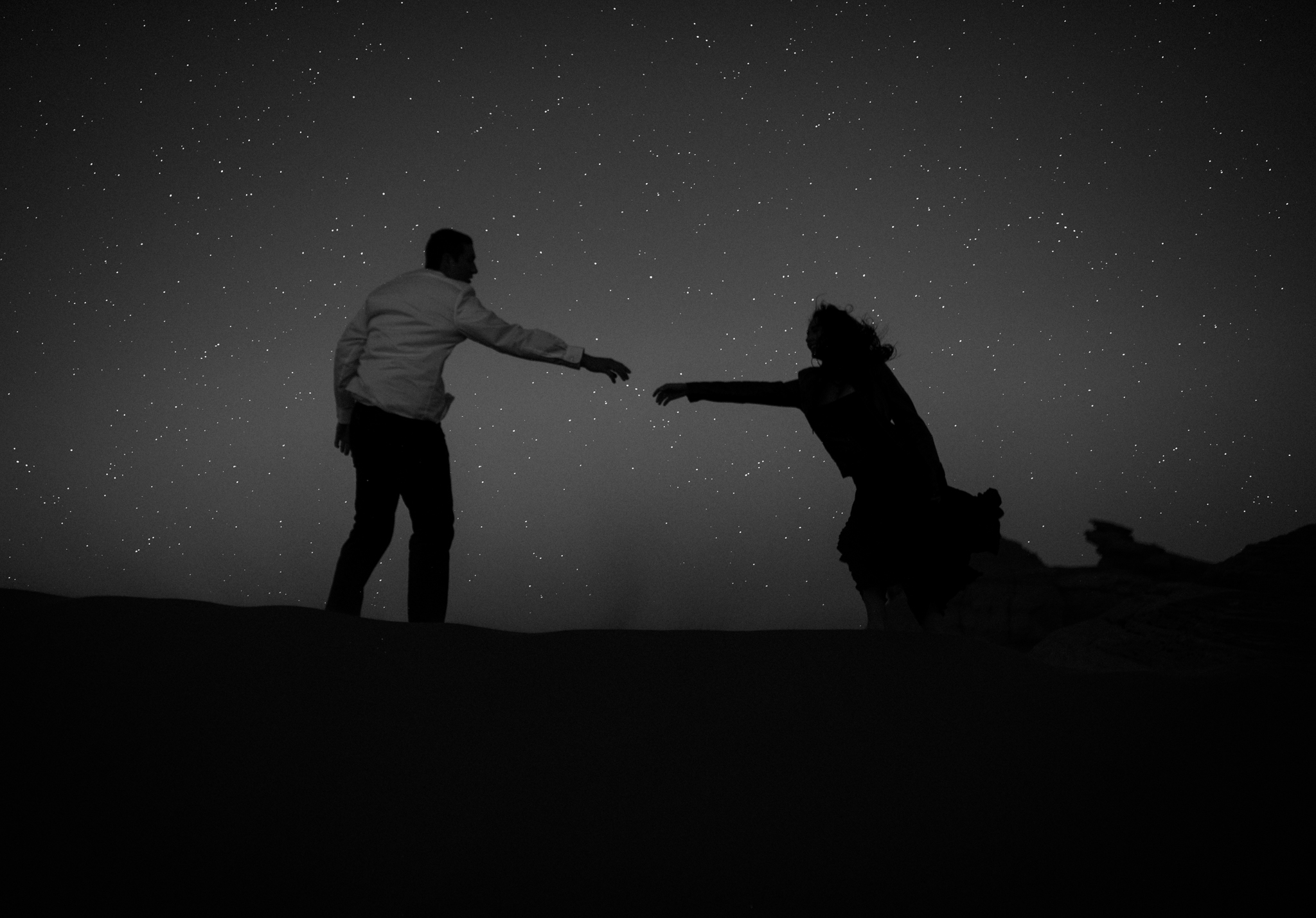 couple reaching for each other at night in front of a starry sky